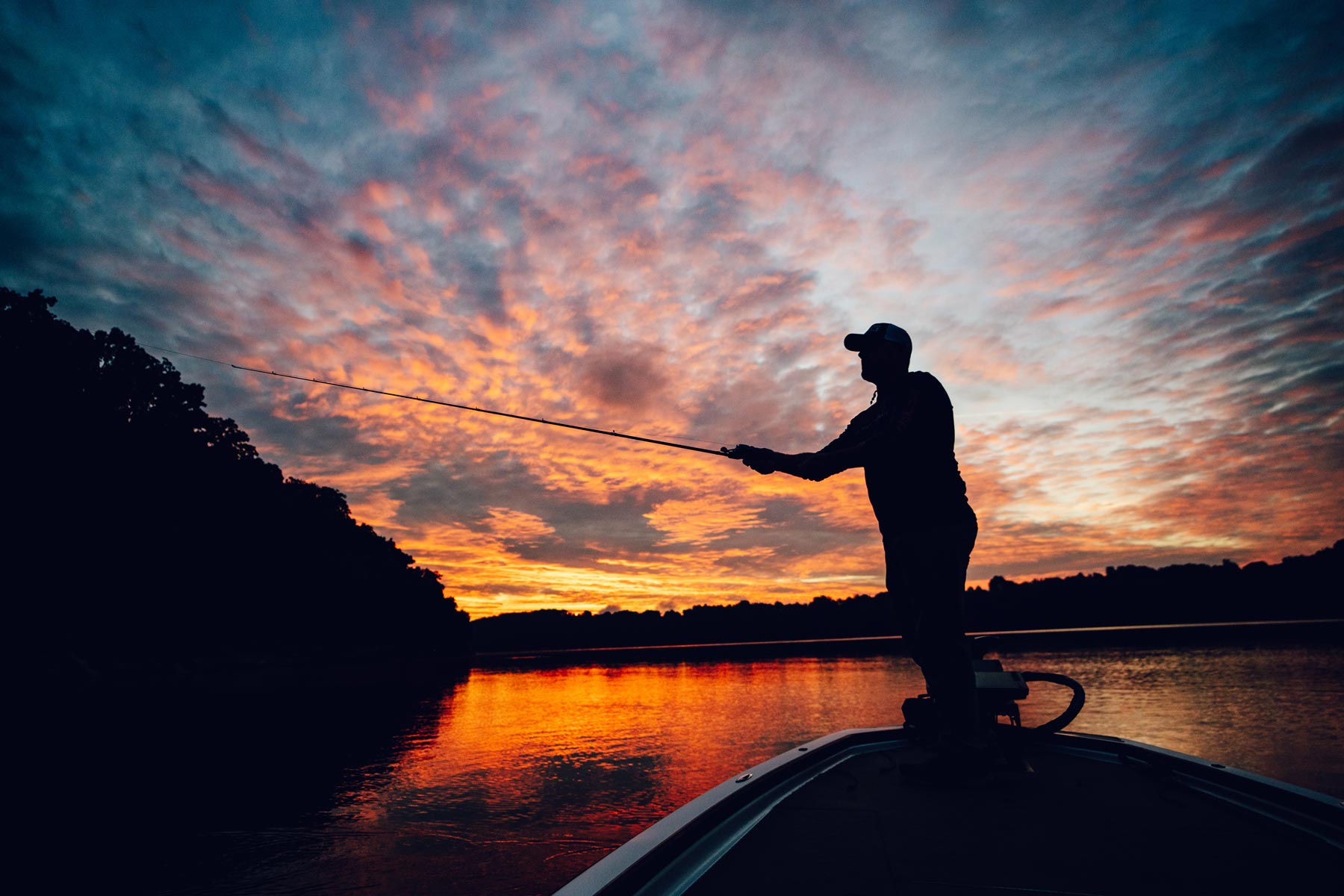 Fisherman in a boat on Lake Cumberland at sunset casting.