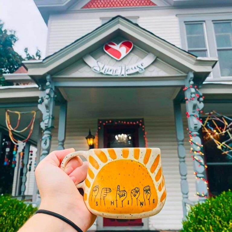 hand holding cup in front of house porch