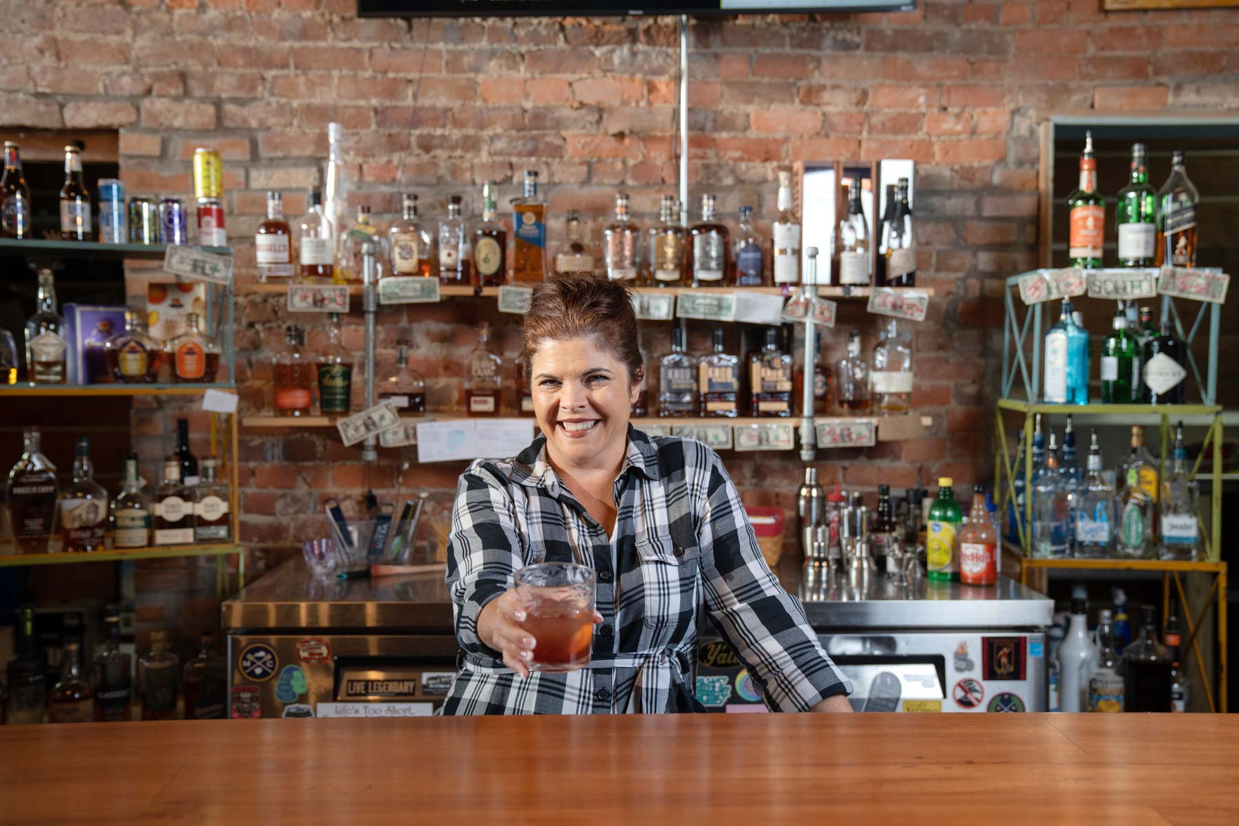 Female bartender behind a bar holding a glass of bourbon