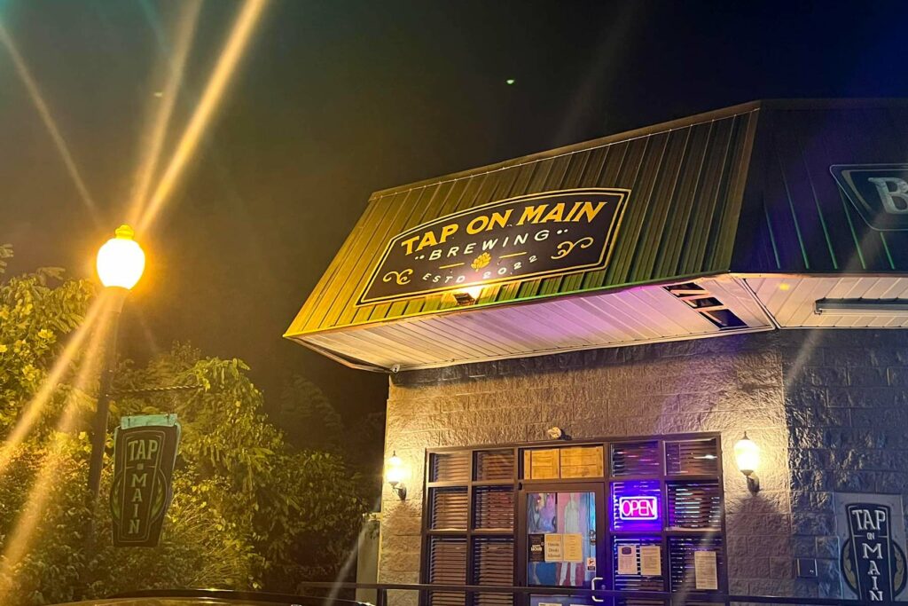 Night view of exterior entrance to building with sign that says Tap On Main.