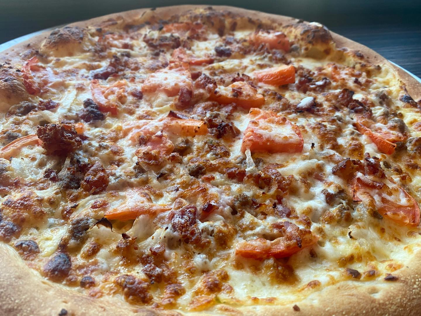 close up of large pizza with meat, tomato, and cheese