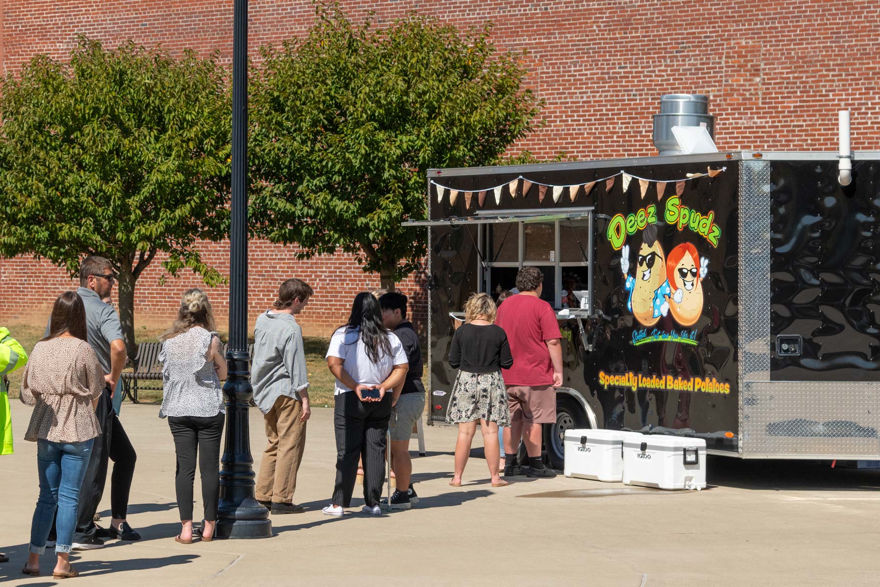people lined up at a food truck with graphics that say "Deez Spudz"