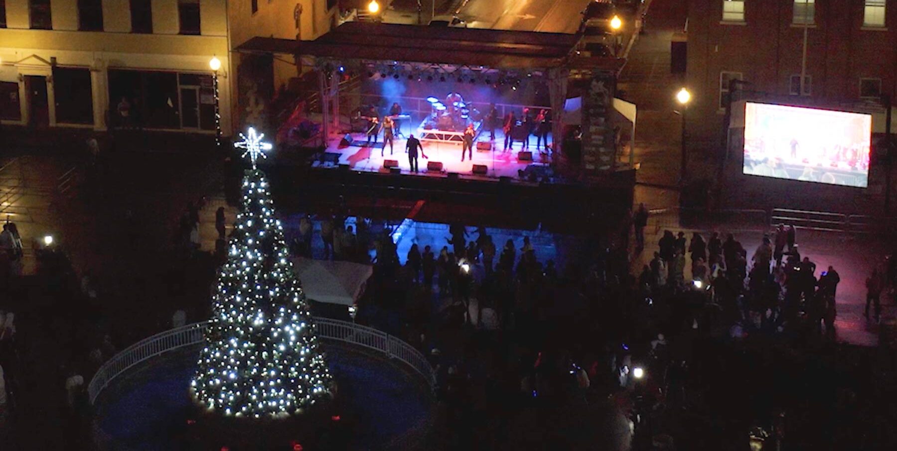 Night view from the sky looking down on a stage with a band and a lighted Christmas tree in Somerset town square.