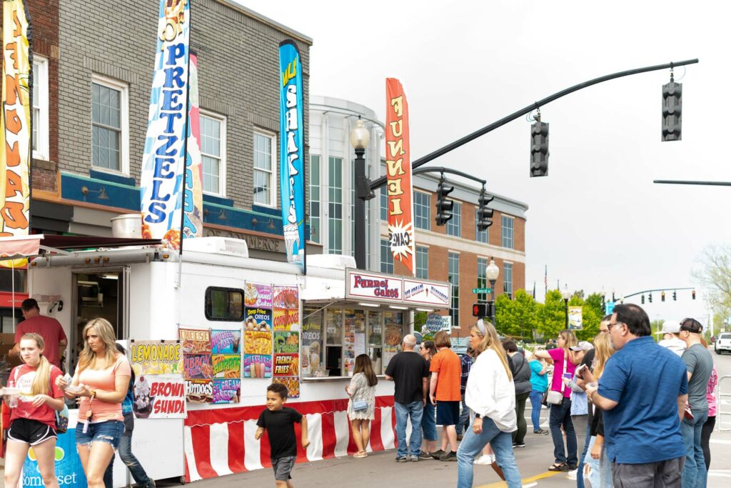 People on the street with Funnel Cake food truck and banners.
