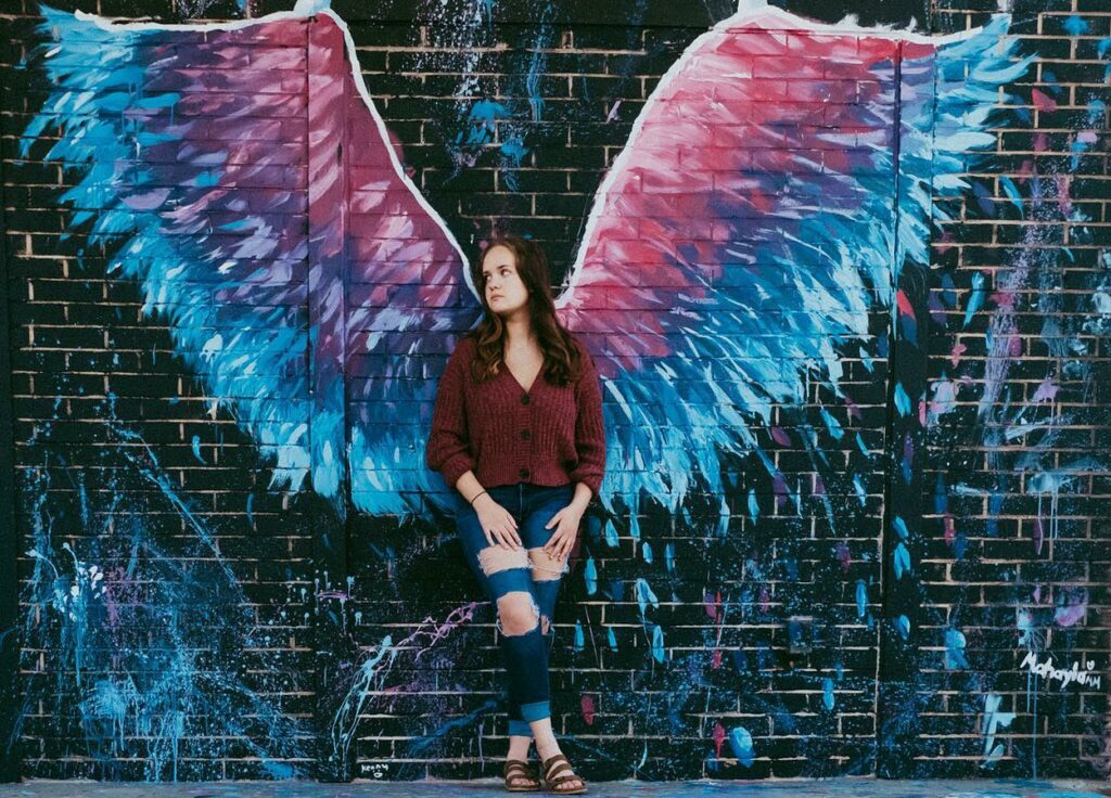 young woman standing in front of wings mural